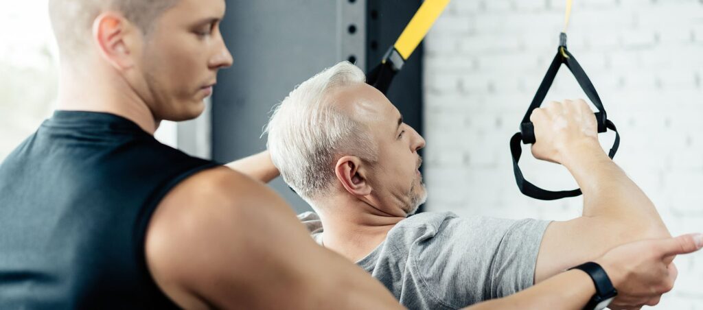Personal trainer at gym showing new resistance exercises to GLP-1 weight loss patient with TRX bands for muscle building